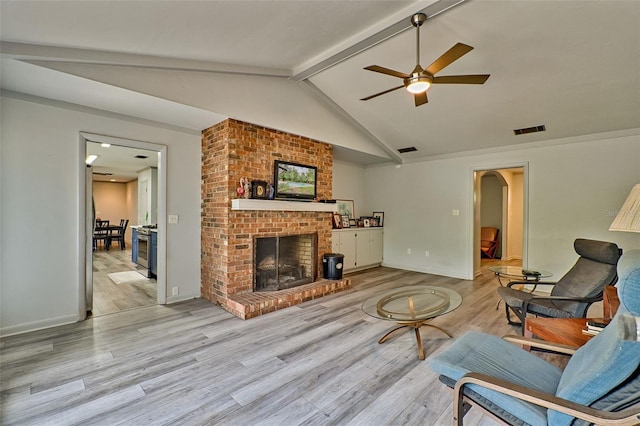 living room featuring ceiling fan, vaulted ceiling with beams, light hardwood / wood-style floors, and a brick fireplace