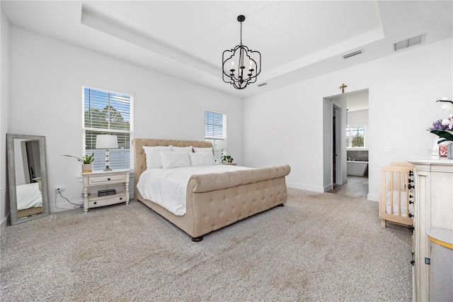 bedroom with a notable chandelier, a tray ceiling, ensuite bathroom, and carpet flooring