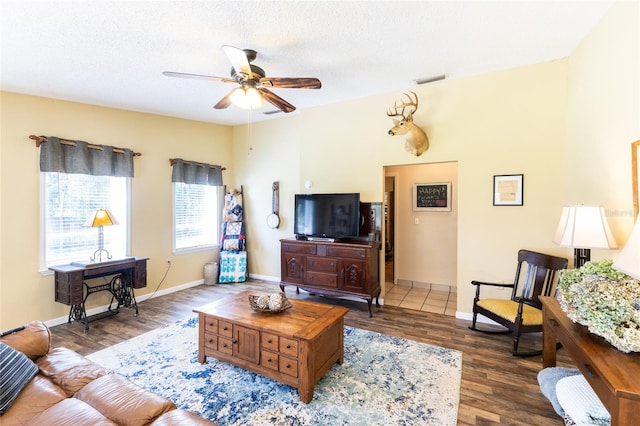 living room with dark wood-type flooring, ceiling fan, and a textured ceiling