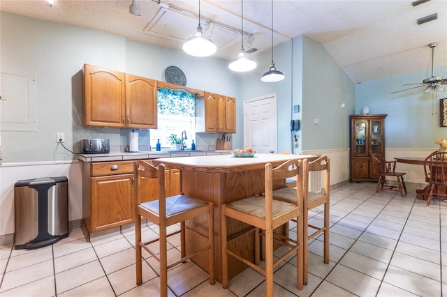 kitchen with vaulted ceiling, a textured ceiling, light tile patterned floors, ceiling fan, and pendant lighting