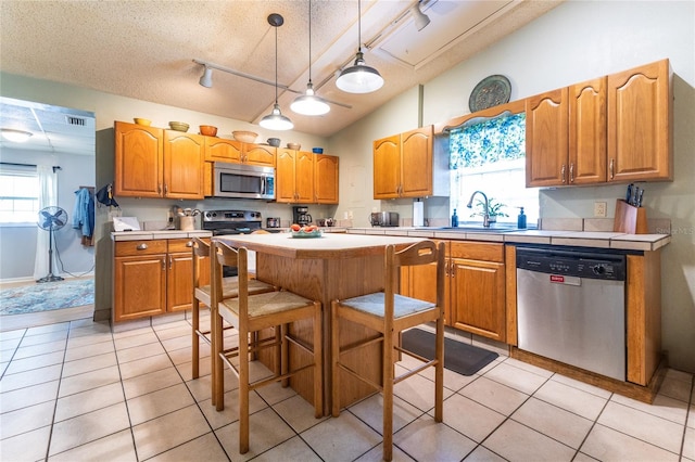 kitchen featuring appliances with stainless steel finishes, rail lighting, a textured ceiling, a center island, and pendant lighting