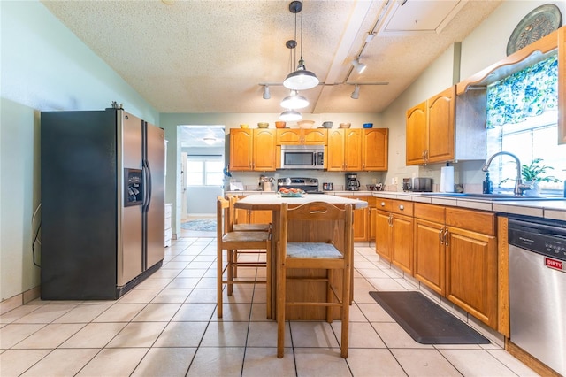 kitchen featuring appliances with stainless steel finishes, a textured ceiling, rail lighting, decorative light fixtures, and a kitchen island