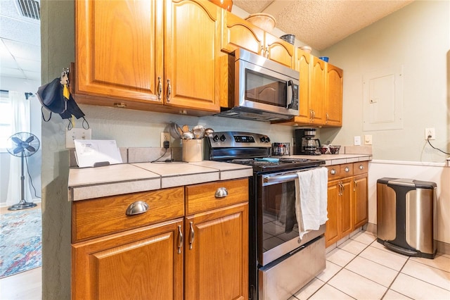 kitchen featuring stainless steel appliances, a textured ceiling, light tile patterned floors, electric panel, and tile counters