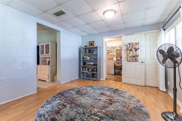 living area with washer and dryer, light hardwood / wood-style flooring, and a drop ceiling