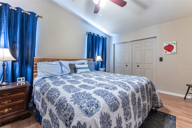 bedroom with a closet, a textured ceiling, hardwood / wood-style floors, vaulted ceiling, and ceiling fan