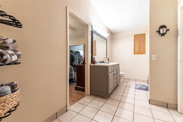 bathroom featuring a textured ceiling, vanity, lofted ceiling, tile patterned floors, and toilet