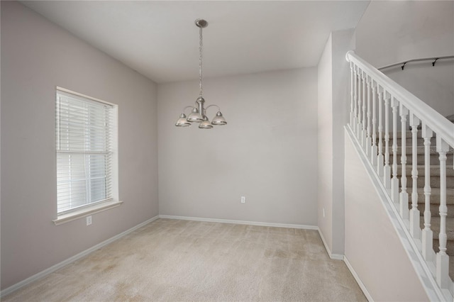 carpeted spare room with a healthy amount of sunlight and an inviting chandelier