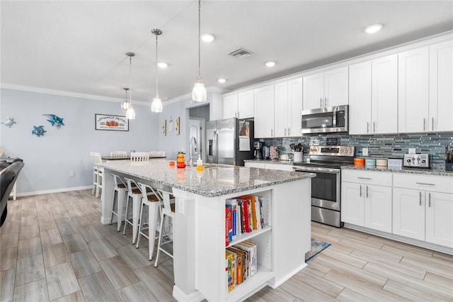 kitchen featuring hanging light fixtures, white cabinets, stainless steel appliances, and a center island with sink