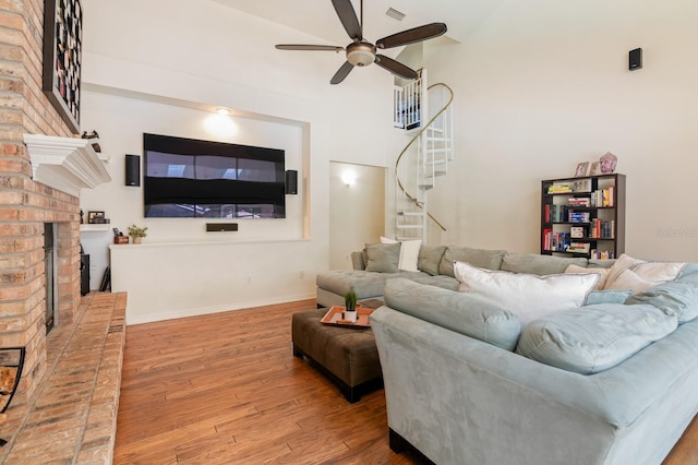 living room featuring a fireplace, wood-type flooring, ceiling fan, and a high ceiling