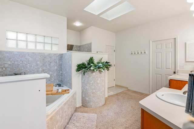 bathroom featuring a skylight, vanity, and a relaxing tiled tub