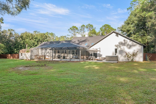 rear view of property featuring glass enclosure, a patio area, a yard, and a hot tub