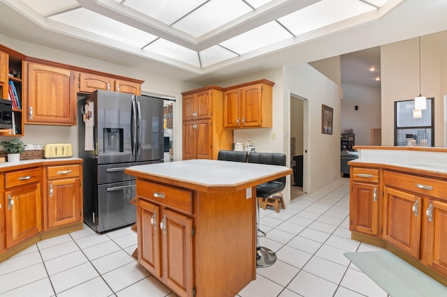 kitchen featuring light tile patterned flooring, a center island, a kitchen breakfast bar, stainless steel fridge with ice dispenser, and hanging light fixtures