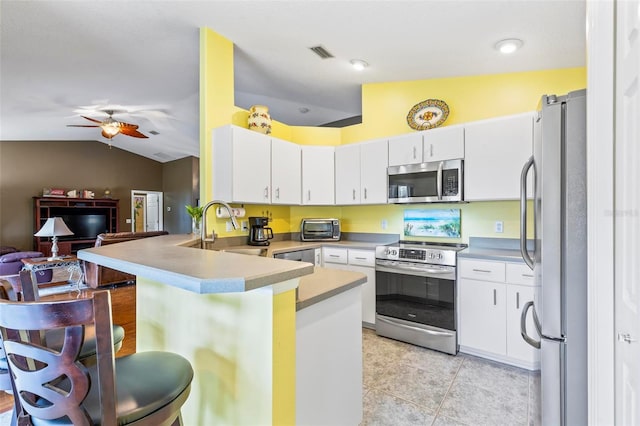 kitchen featuring vaulted ceiling, a breakfast bar area, appliances with stainless steel finishes, kitchen peninsula, and white cabinets