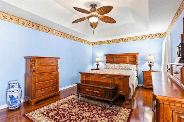 bedroom featuring a raised ceiling, ceiling fan, and dark wood-type flooring