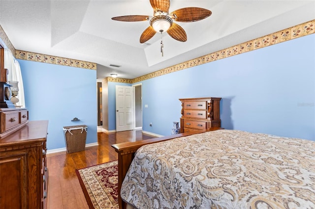 bedroom featuring ceiling fan, a tray ceiling, and dark wood-type flooring