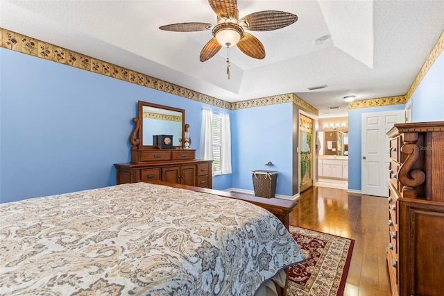 bedroom with a textured ceiling, a raised ceiling, hardwood / wood-style floors, connected bathroom, and ceiling fan