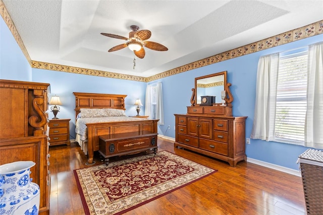 bedroom featuring ceiling fan, dark wood-type flooring, a raised ceiling, and a textured ceiling