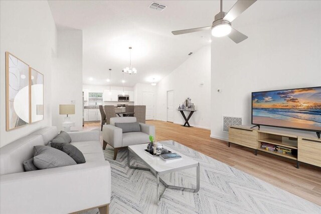 living room featuring high vaulted ceiling, light wood-type flooring, and ceiling fan with notable chandelier