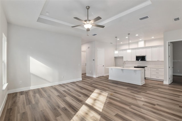 kitchen with tasteful backsplash, white cabinetry, decorative light fixtures, hardwood / wood-style flooring, and an island with sink