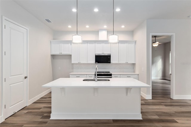 kitchen with pendant lighting, sink, white cabinets, dark wood-type flooring, and a kitchen island with sink