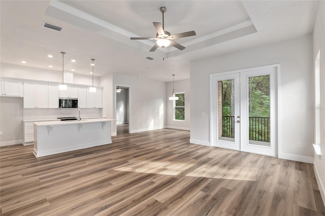 unfurnished living room featuring french doors, sink, ceiling fan, a raised ceiling, and light wood-type flooring