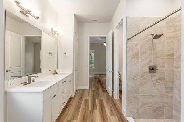 bathroom featuring wood-type flooring, a tile shower, vanity, toilet, and ceiling fan