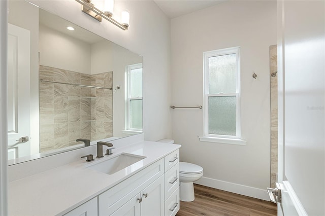 bathroom with wood-type flooring, vanity, toilet, and tiled shower