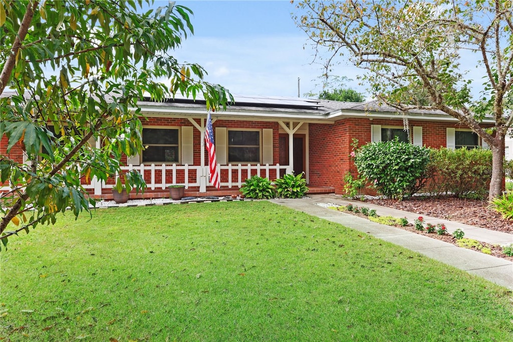 ranch-style home with a front yard, solar panels, and a porch