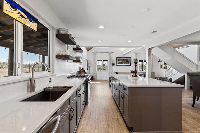 kitchen featuring light stone counters, sink, light hardwood / wood-style flooring, a center island, and stainless steel range with gas cooktop