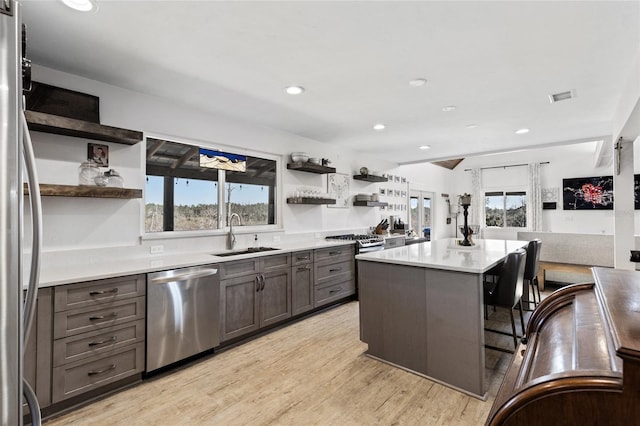 kitchen with a center island, sink, light wood-type flooring, appliances with stainless steel finishes, and a healthy amount of sunlight