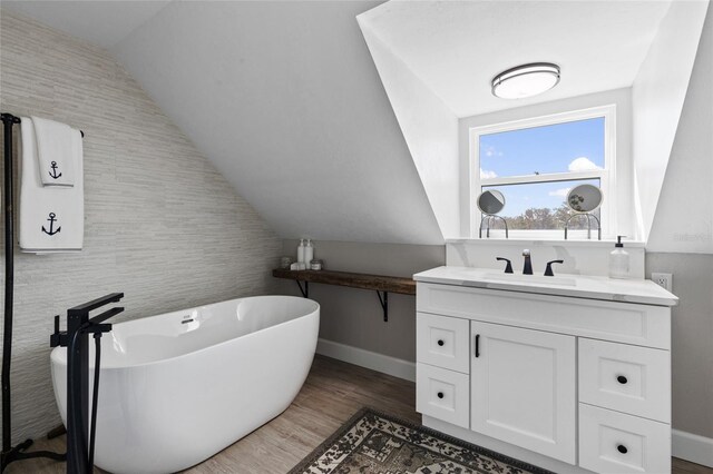 bathroom with hardwood / wood-style flooring, vanity, a bath, and vaulted ceiling