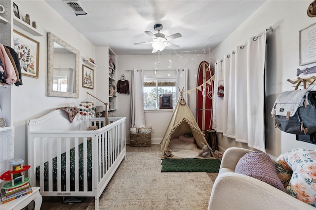 bedroom with ceiling fan, a nursery area, and hardwood / wood-style flooring