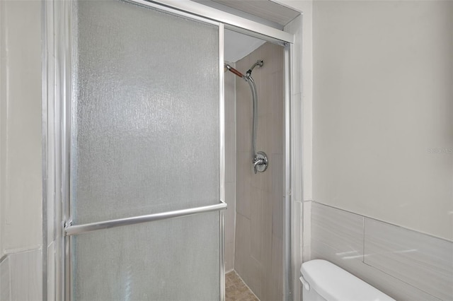 bathroom with toilet, tile walls, and a shower with door