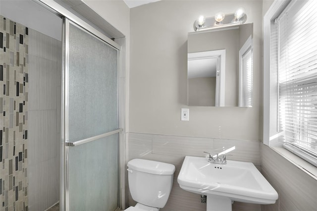 bathroom featuring a wealth of natural light, a shower with door, sink, tile walls, and toilet