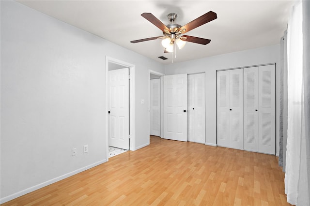 unfurnished bedroom with visible vents, baseboards, a ceiling fan, light wood-type flooring, and two closets