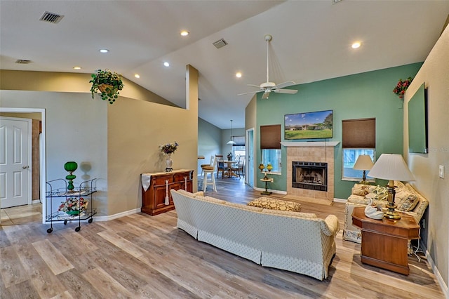 living room featuring ceiling fan, light hardwood / wood-style floors, lofted ceiling, and a tile fireplace