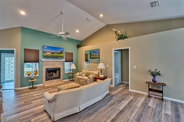 living room featuring a tile fireplace, ceiling fan, hardwood / wood-style floors, and high vaulted ceiling