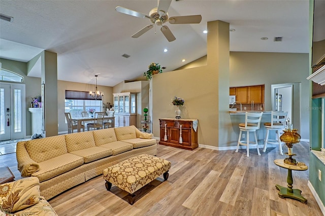 living room with ceiling fan with notable chandelier, light hardwood / wood-style floors, and high vaulted ceiling