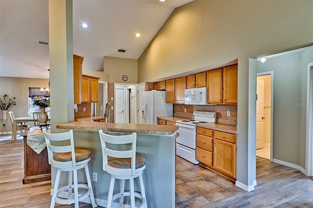 kitchen featuring kitchen peninsula, a kitchen bar, tasteful backsplash, white appliances, and light hardwood / wood-style floors