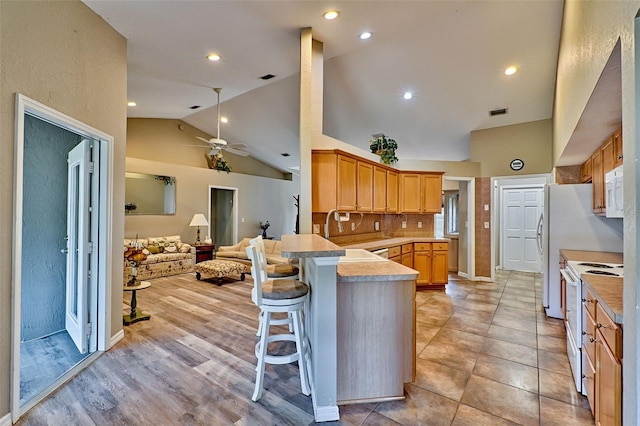 kitchen featuring kitchen peninsula, white appliances, sink, light hardwood / wood-style floors, and a breakfast bar area