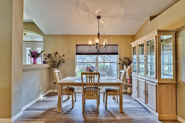 dining room featuring hardwood / wood-style floors, a healthy amount of sunlight, vaulted ceiling, and a notable chandelier