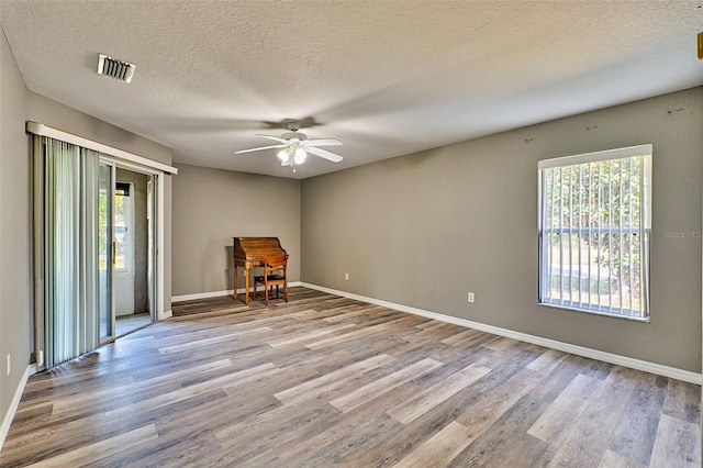 empty room featuring a textured ceiling, light hardwood / wood-style flooring, a wealth of natural light, and ceiling fan