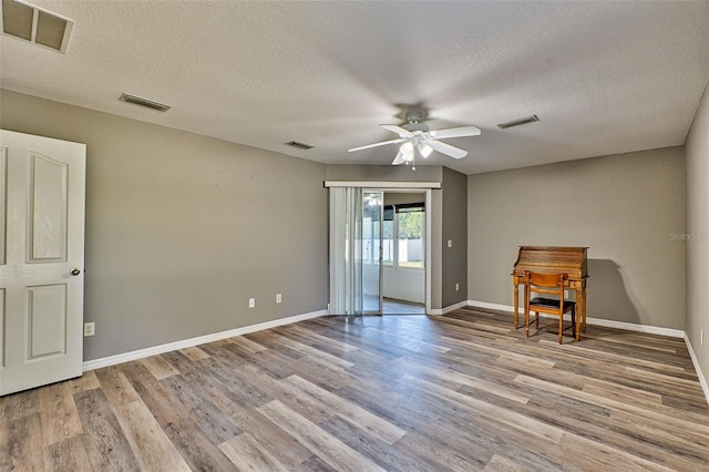 unfurnished room with a textured ceiling, light wood-type flooring, and ceiling fan