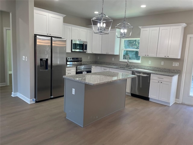 kitchen with a center island, white cabinets, sink, light stone countertops, and stainless steel appliances