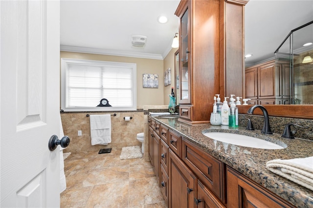 bathroom with vanity, a shower with door, toilet, ornamental molding, and tile walls