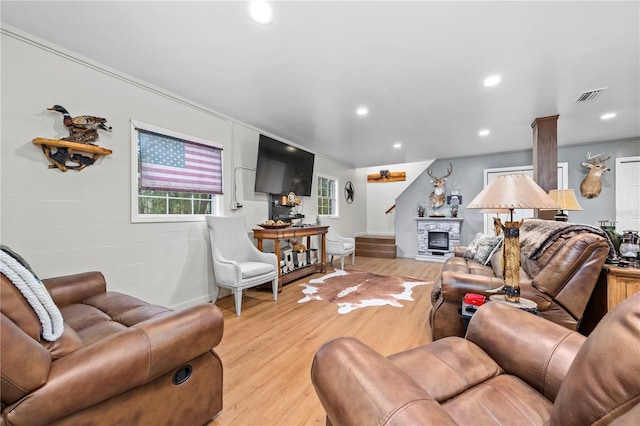 living room featuring a stone fireplace, light wood-type flooring, and ornate columns