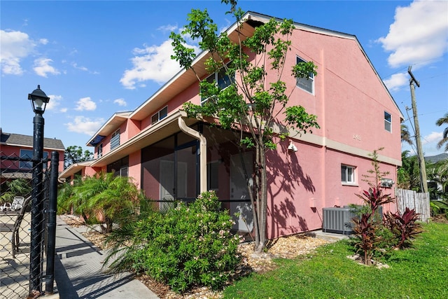 13433 Heald Ln Unit 1A, Fort Myers, FL 33908 - view of property exterior featuring stucco siding, central AC unit, fence, and a sunroom