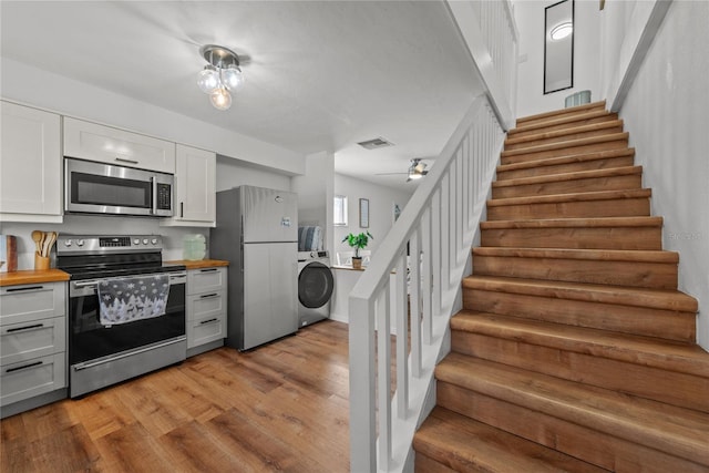 kitchen featuring white cabinetry, wood counters, light hardwood / wood-style flooring, washer / dryer, and appliances with stainless steel finishes