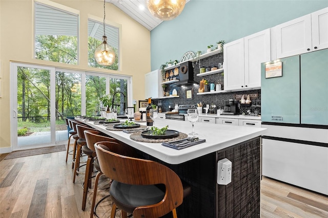 kitchen featuring a kitchen island with sink, decorative light fixtures, high vaulted ceiling, light hardwood / wood-style flooring, and white cabinetry