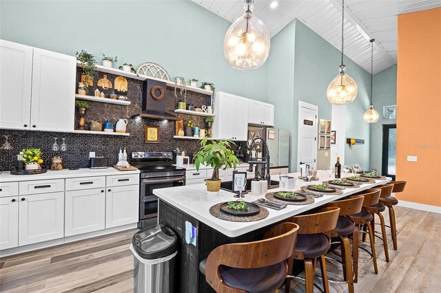 kitchen featuring white cabinets, decorative light fixtures, stainless steel appliances, and a center island with sink